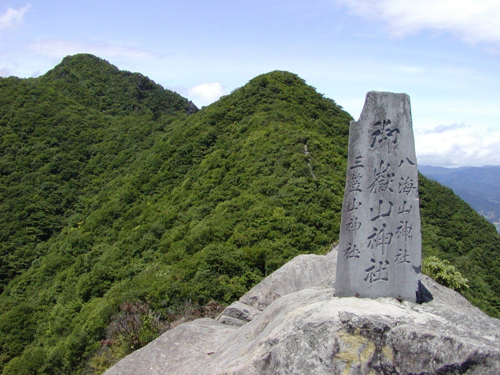 A stone monument with inscriptions on a mountain peak surrounded by dense green forest.