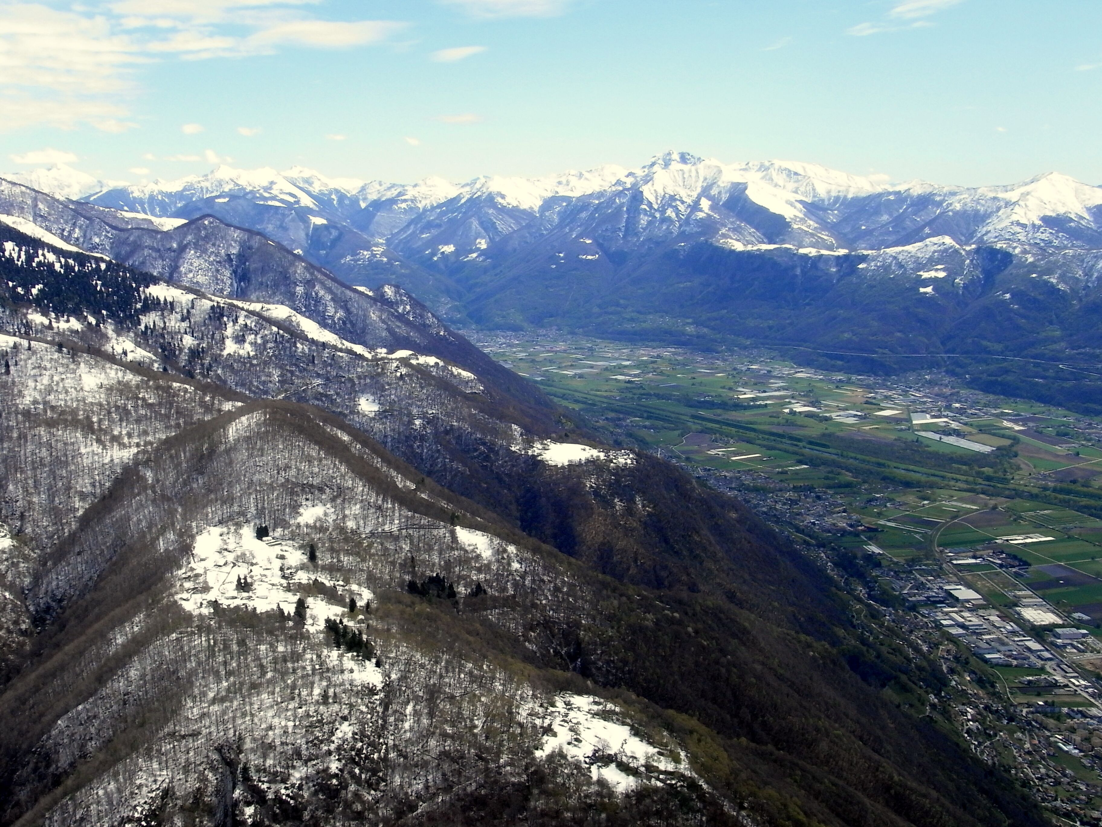 A mountainous landscape with snow-capped peaks, a valley with agricultural fields, and a small town.