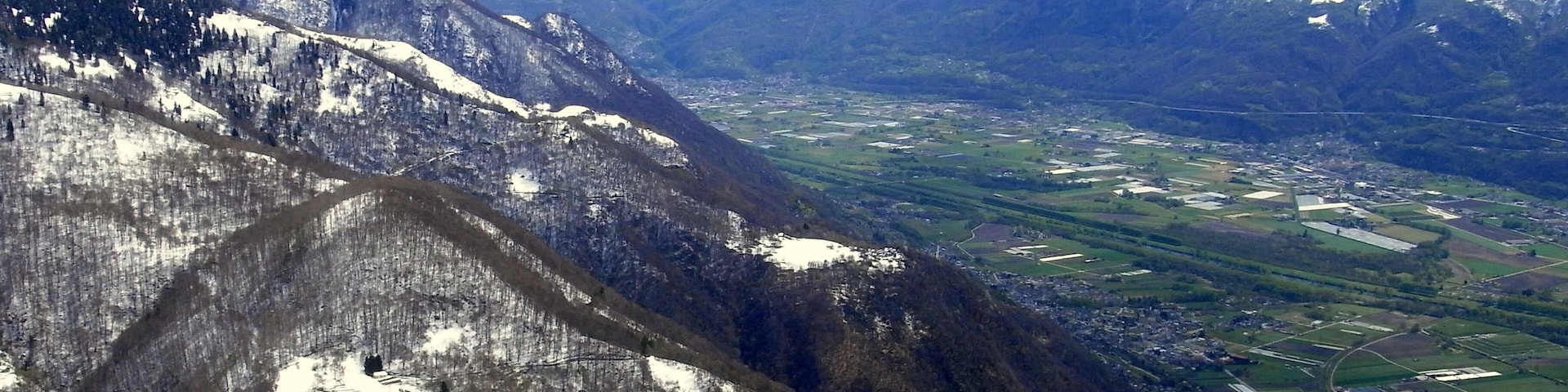 Un paisaje montañoso con picos nevados, un valle con campos de cultivo y un pequeño pueblo.