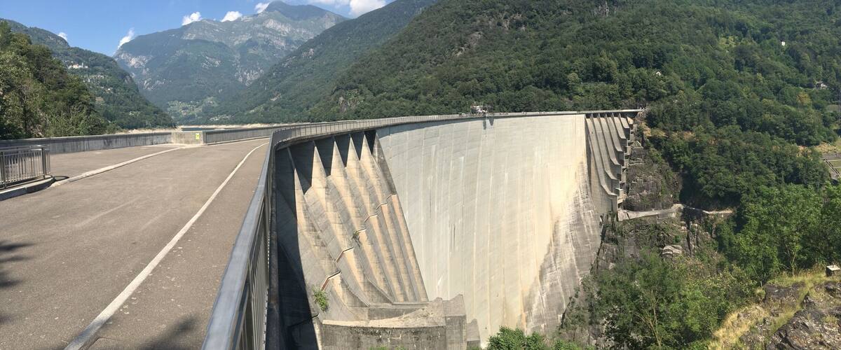 A large dam with a road running alongside it, surrounded by lush green mountains.