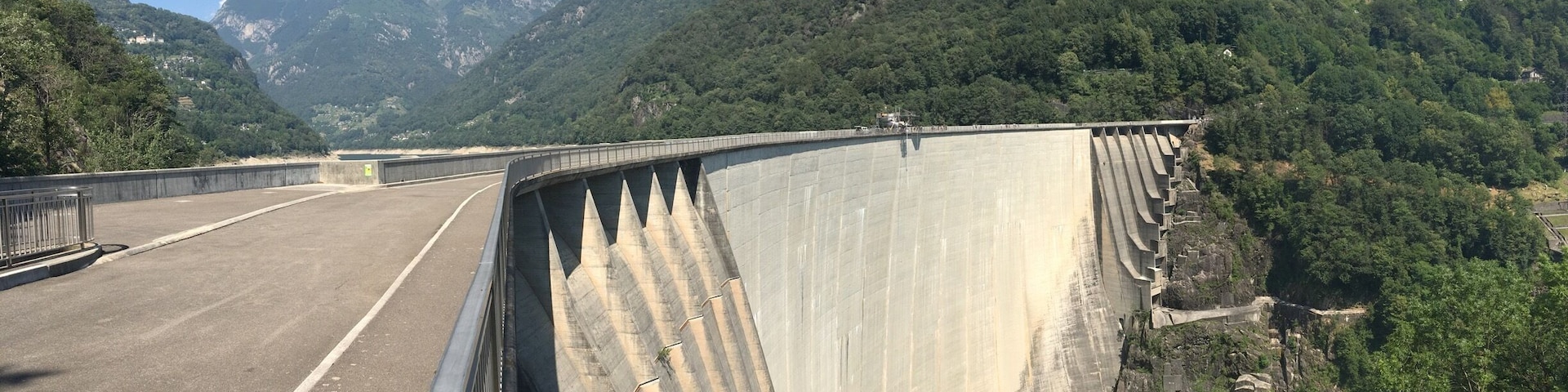 A large dam with a road running alongside it, surrounded by lush green mountains.