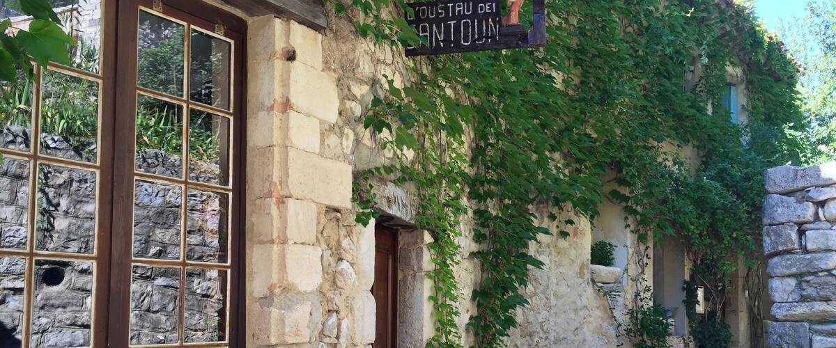 A stone building with a sign reading "Oustau des Antoins" and a cobblestone path.