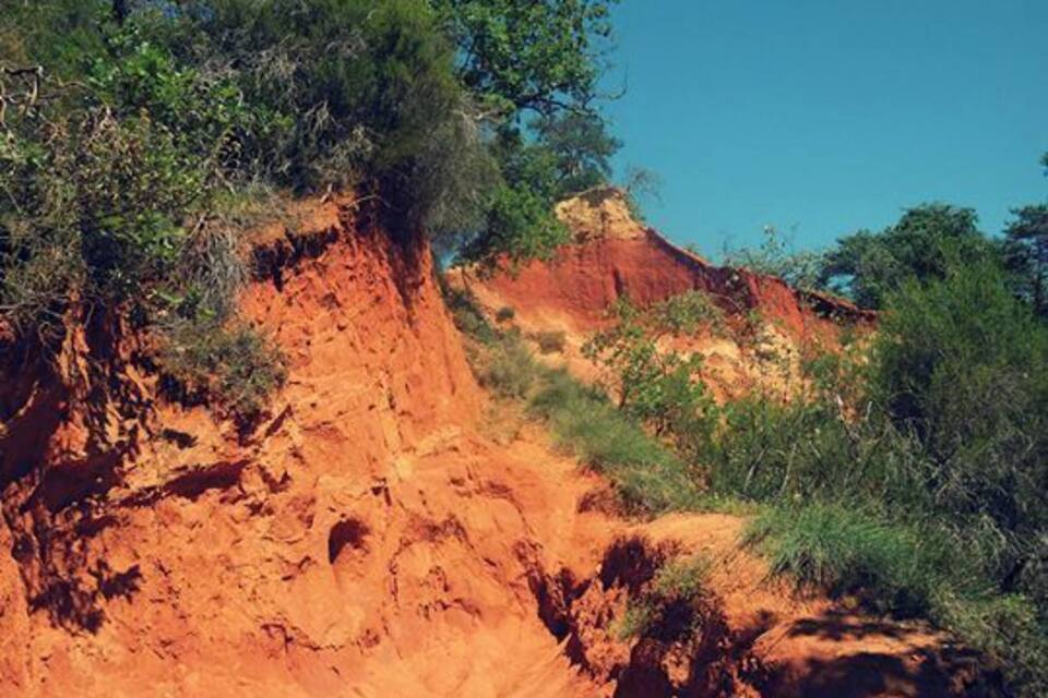 A red sandstone cliff with sparse vegetation and a clear blue sky.