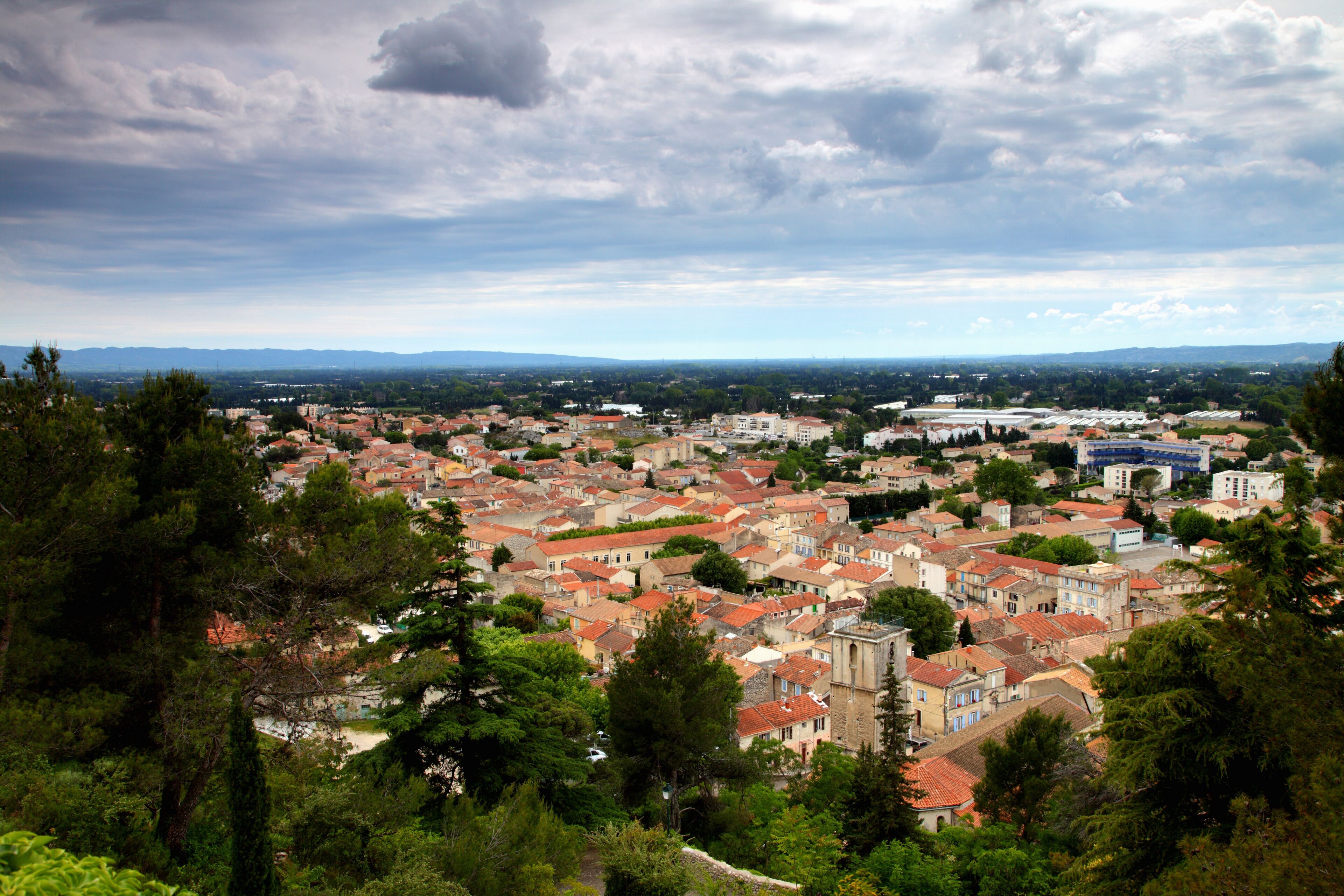 A town with red-roofed buildings, surrounded by greenery and mountains in the background.