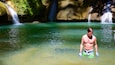 Un hombre en una piscina poco profunda y cristalina, con una cascada al fondo.