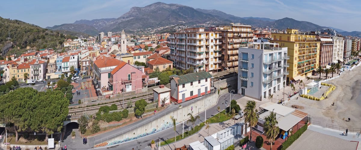 A coastal town with colorful buildings, a beach, and mountains in the background.