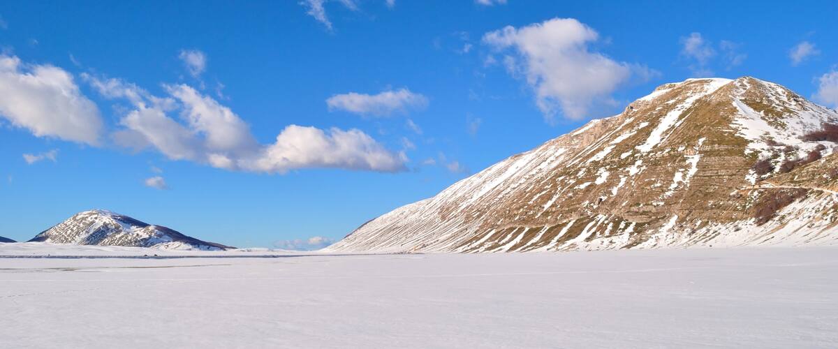 A snow-covered landscape with a prominent mountain and a clear blue sky.