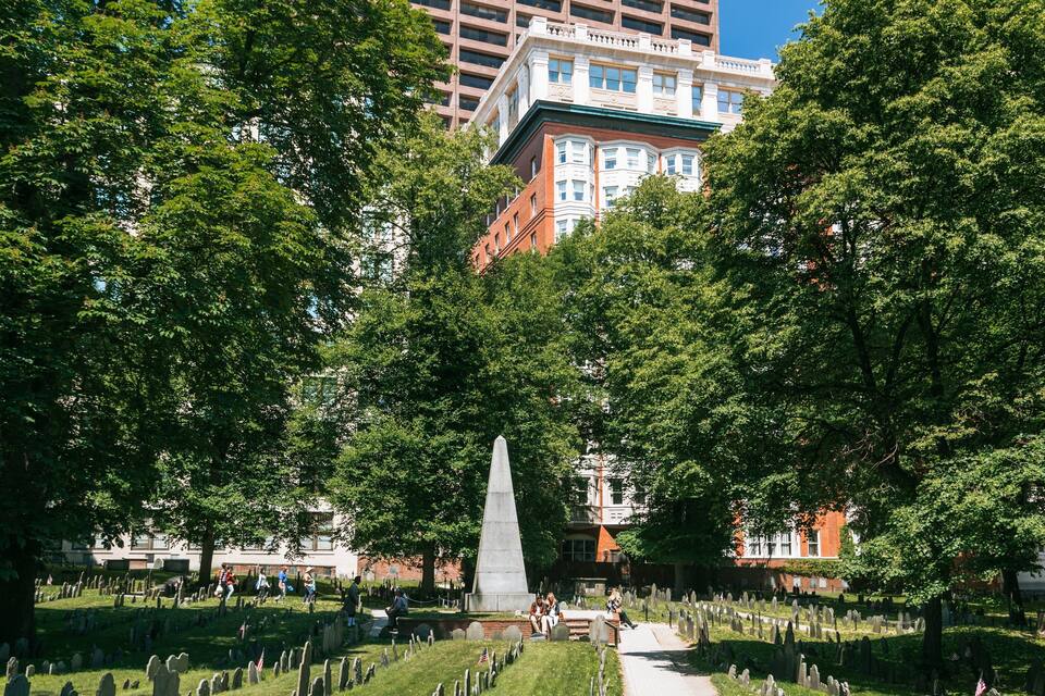 Een kerkhof met grafstenen, een centraal monument en omliggende bomen.