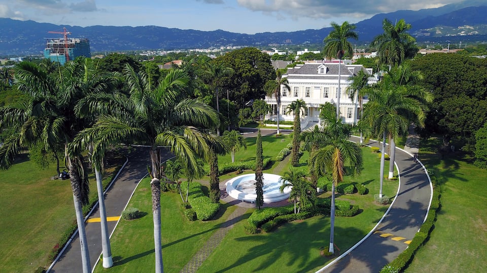A landscaped area with palm trees, a curved road, and a white building with columns.