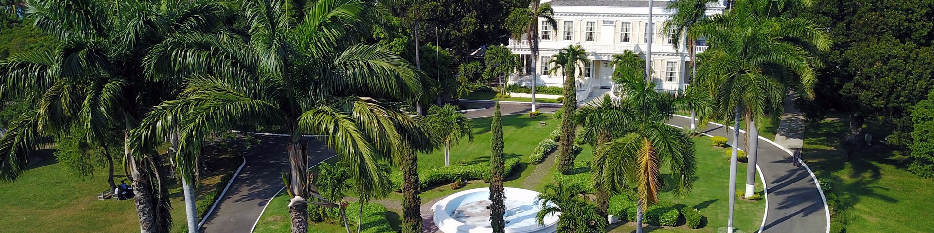 Un área ajardinada con palmeras, una carretera curva y un edificio blanco con columnas.