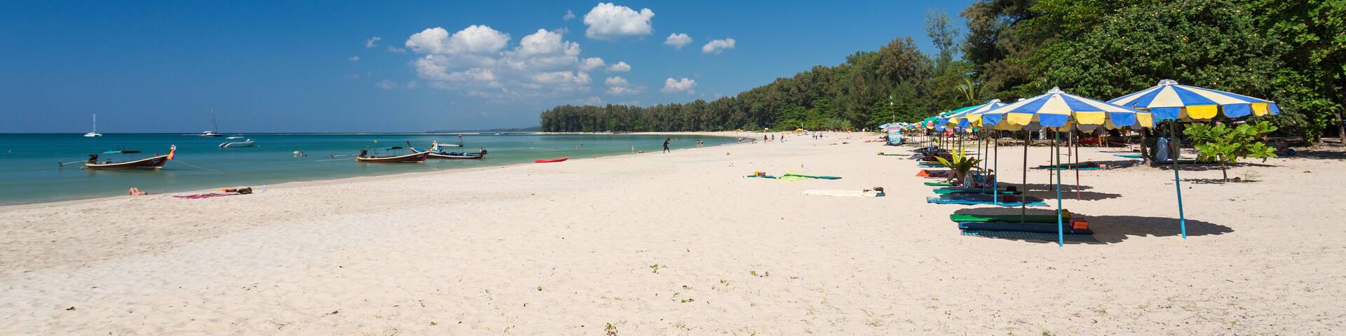 A beach with clear blue water, boats, and umbrellas.