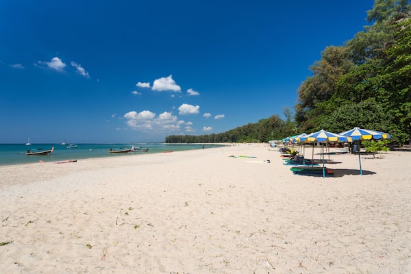 A beach with clear blue water, boats, and umbrellas.