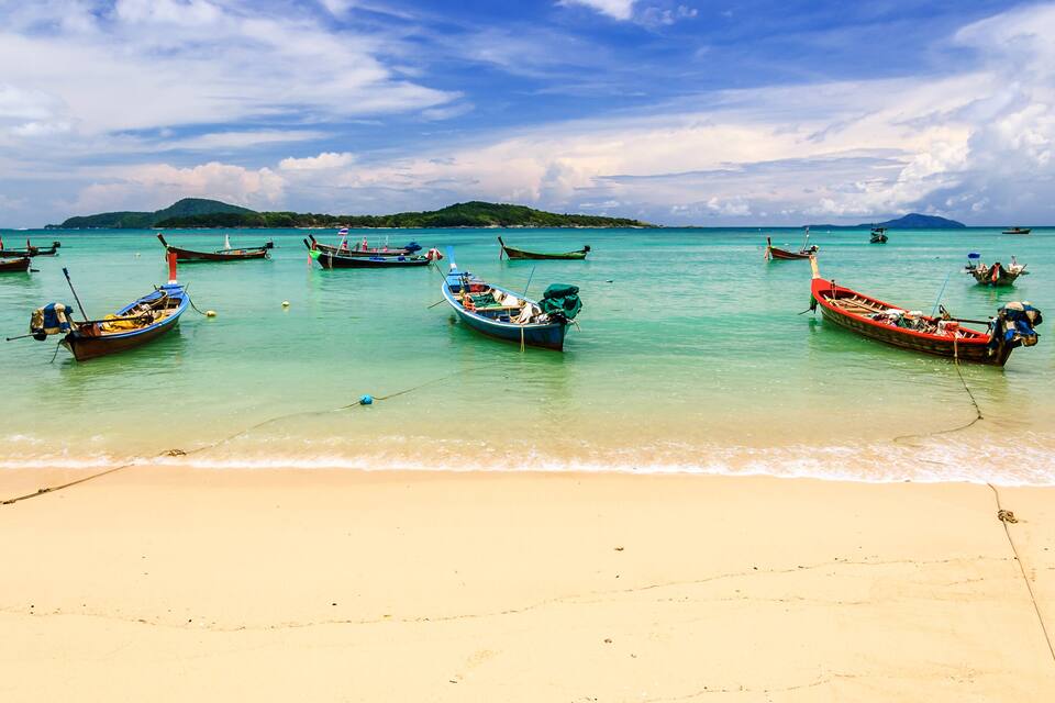 A beach with several traditional boats anchored in calm turquoise waters.