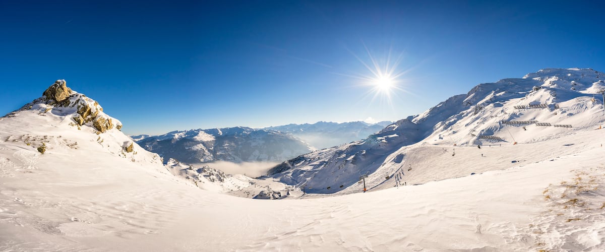 A snow-covered mountain landscape with a clear sky and the sun shining brightly.