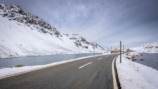A snow-covered road curving alongside a lake with mountains in the background.