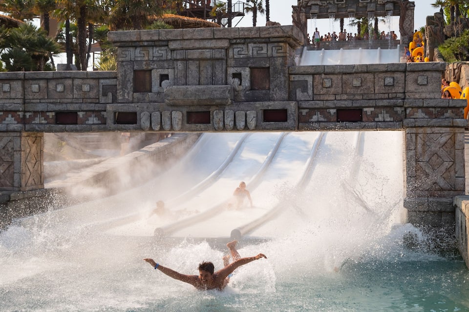 Eine Wasserrutsche in einem Freizeitpark mit einer Steinstruktur und Wasser, das die Rutsche hinabspült.