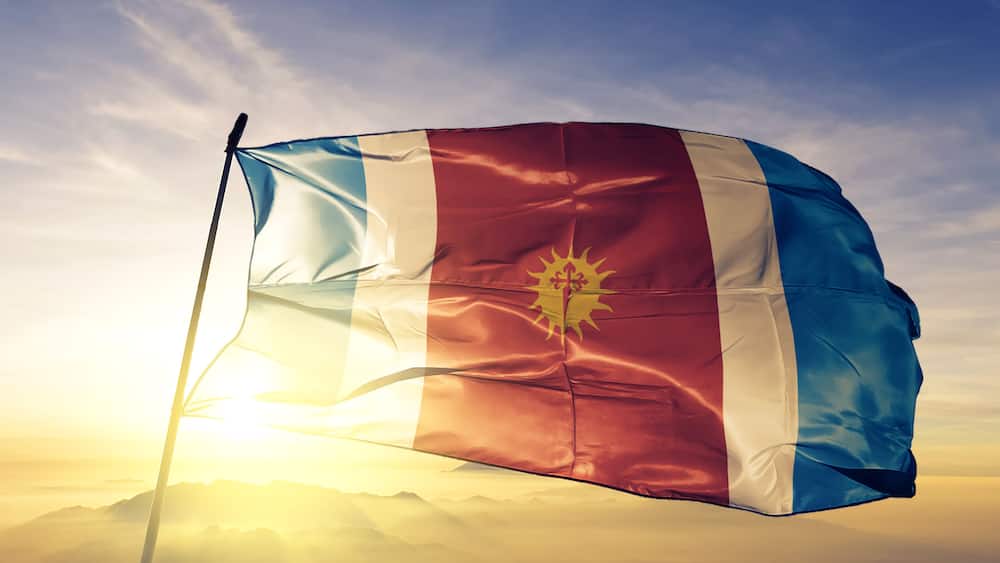 A flag waving against a clear sky with a sunlit mountain range in the background.