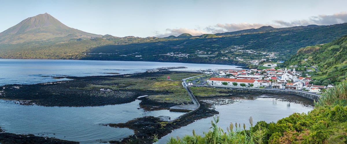 A coastal town with a prominent mountain in the background, a harbor with boats, and a bridge connecting the town to the mainland.