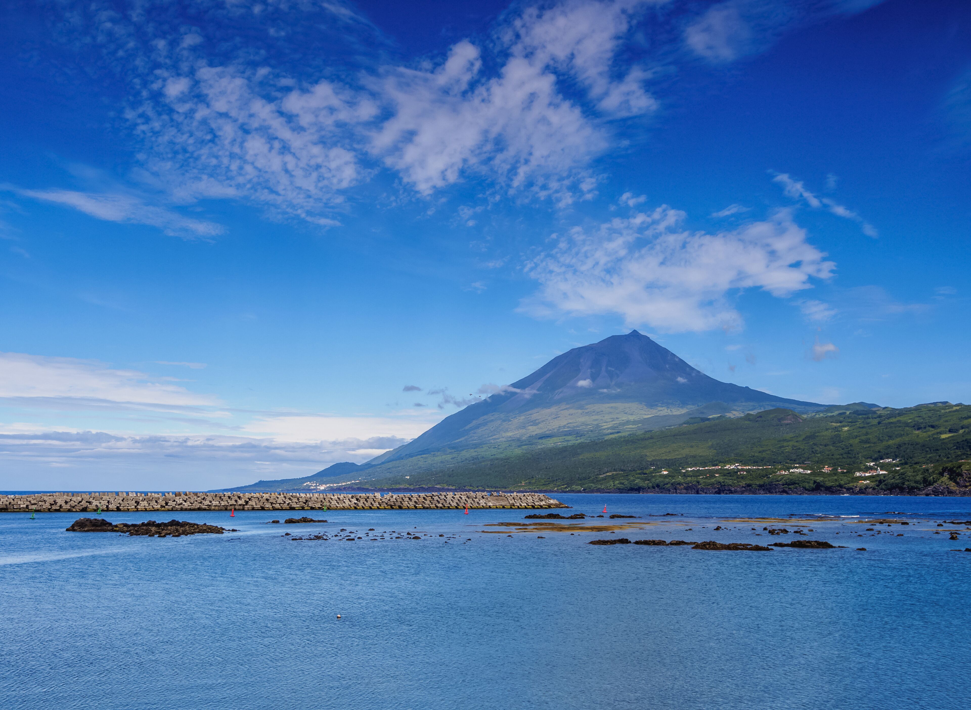 A coastal landscape with a prominent mountain, clear blue sky, and calm sea.