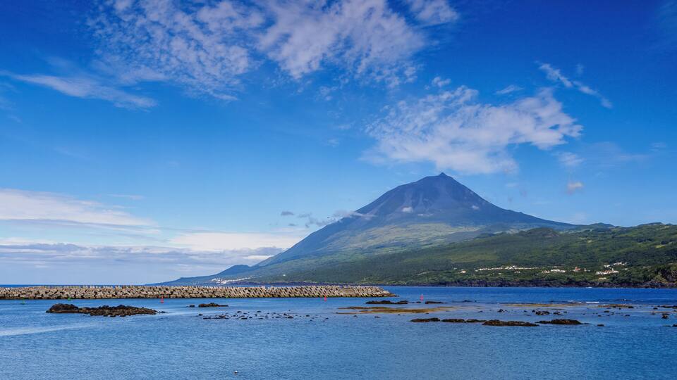 A coastal landscape with a prominent mountain, clear blue sky, and calm sea.