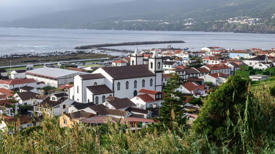 A coastal town with white buildings, a church, and a rocky breakwater.