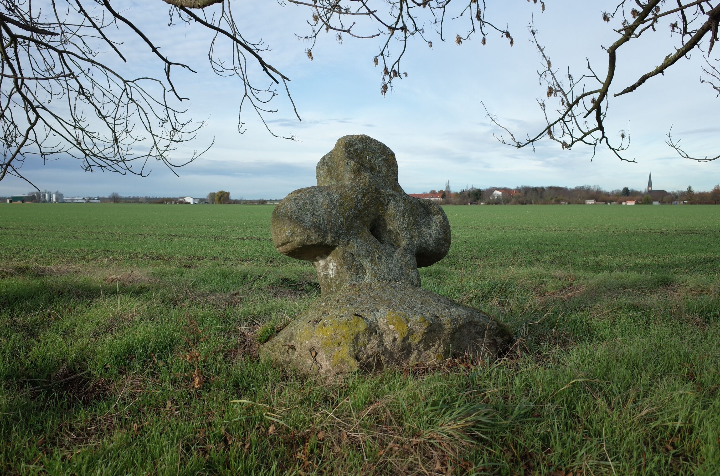 A large stone sculpture in a grassy field with a church in the background.