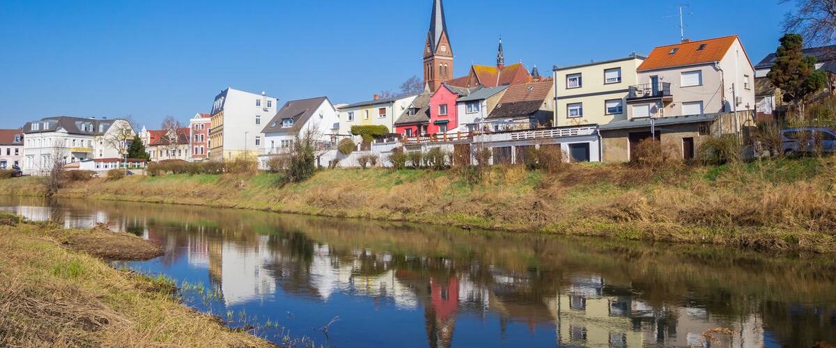 A river with a church and residential buildings on the opposite bank.