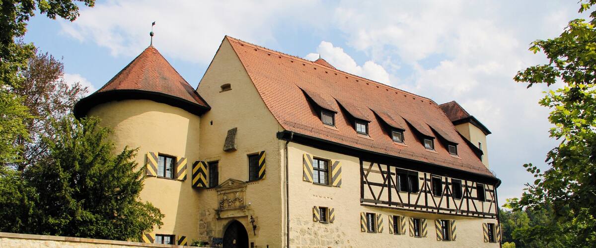 A historic building with a red-tiled roof, a round tower, and a stone bridge.