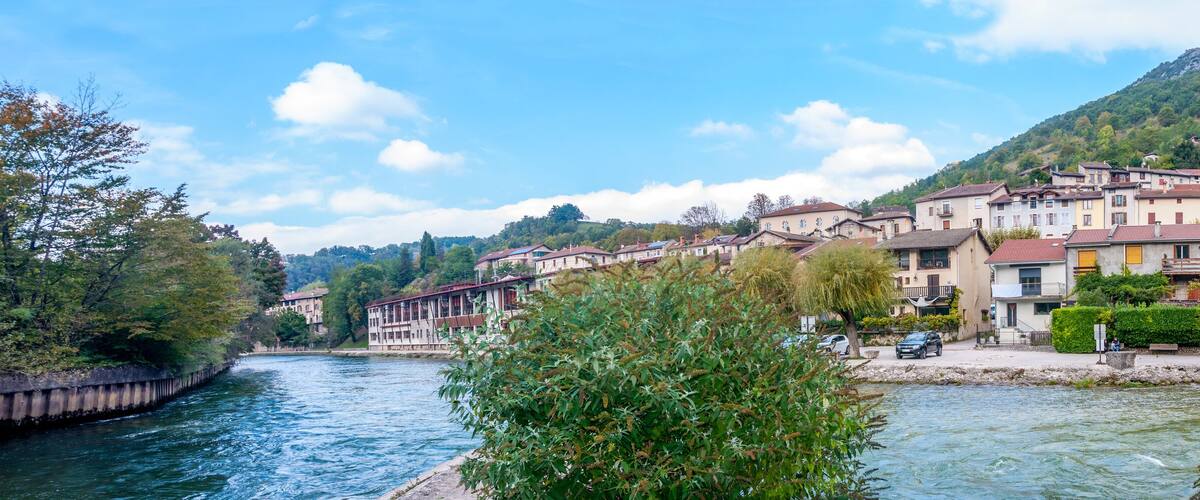 A riverside town with historic buildings, a church, and a mountain backdrop.