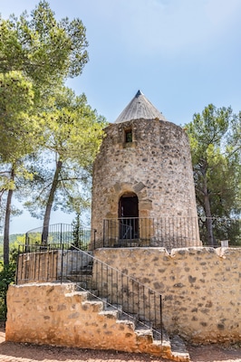Una torre de piedra con techo cónico, rodeada de árboles y una barandilla metálica.