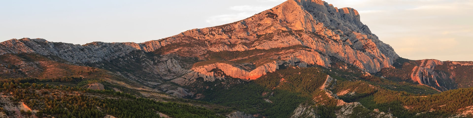 A rugged mountain range with a prominent peak, dense forested valleys, and a small lake.