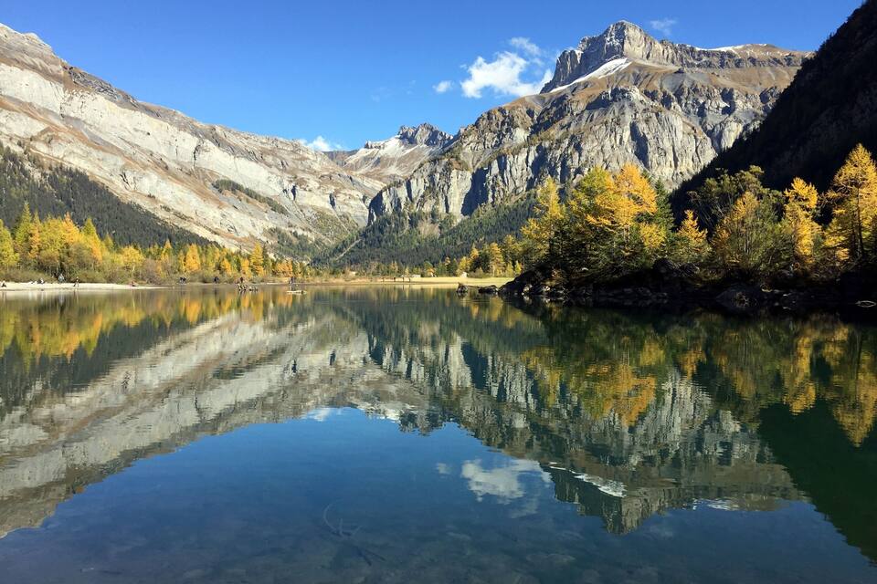Un lago tranquilo que refleja montañas y árboles de colores otoñales.