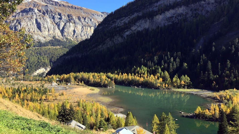 Un paysage montagneux avec un lac, des arbres aux couleurs automnales et un petit village.