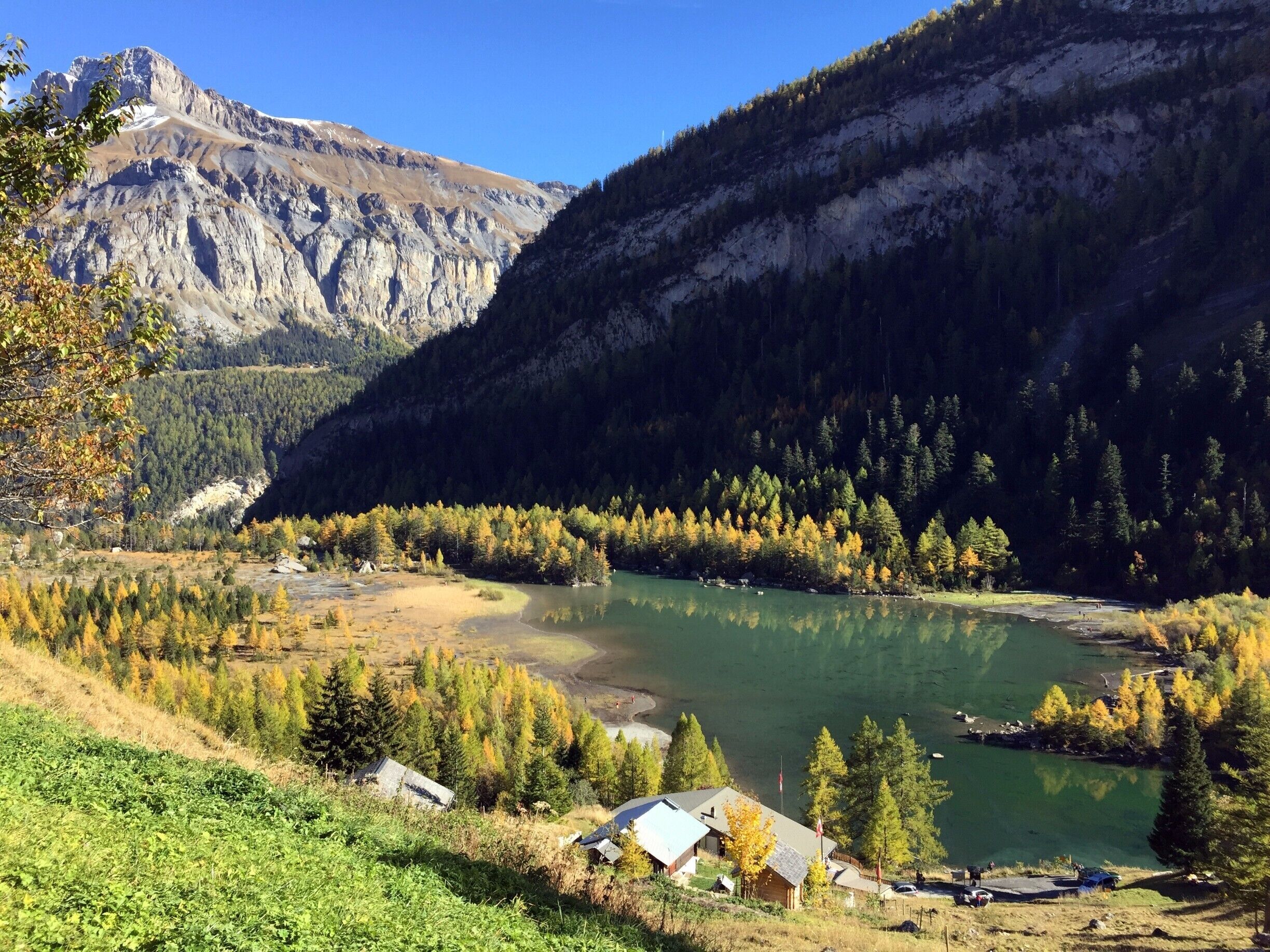 A mountainous landscape with a lake, autumn-colored trees, and a small settlement.