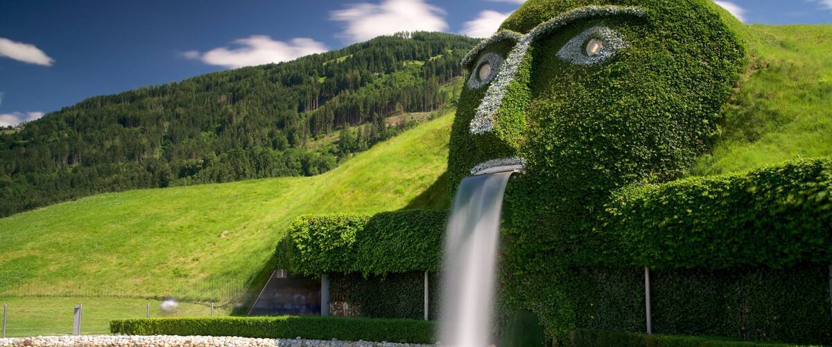A mountain landscape with a waterfall cascading down a hedge shaped like a face.