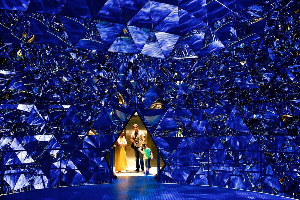 Een geometrisch bouwwerk met reflecterende oppervlakken en een centrale doorgang.
