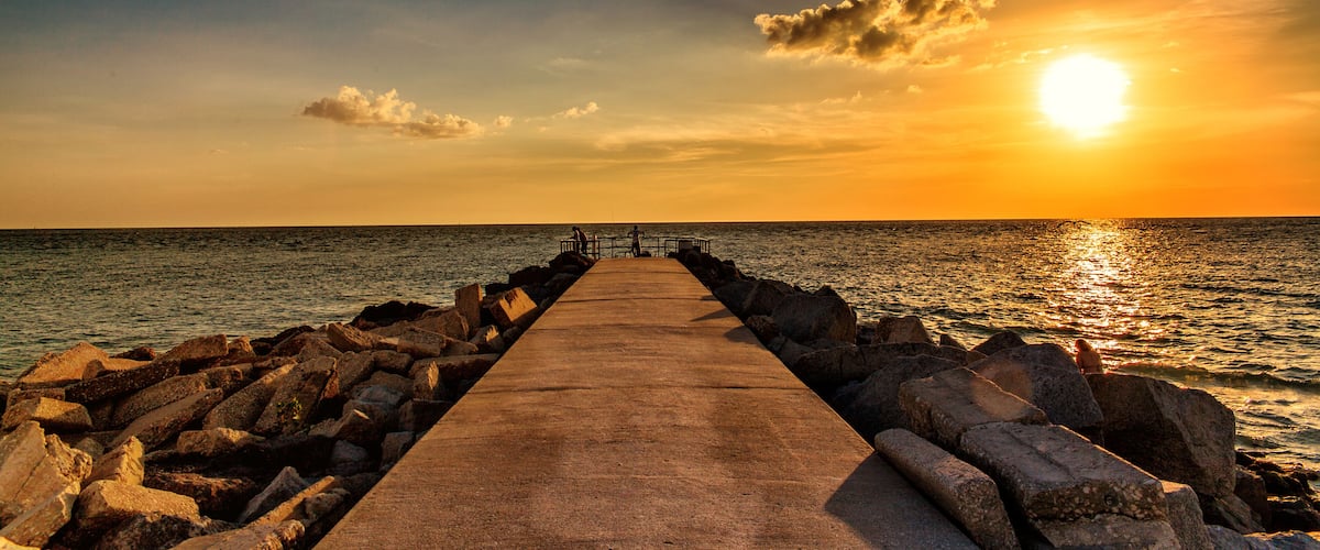 A pier extending into the sea at sunset with a clear sky.