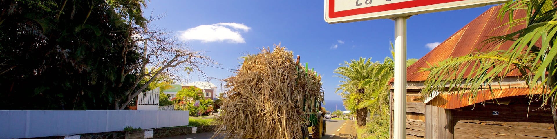 A rural road with a truck carrying a large load of sugarcane. A sign indicates the location as Petite Île, La Croisée.