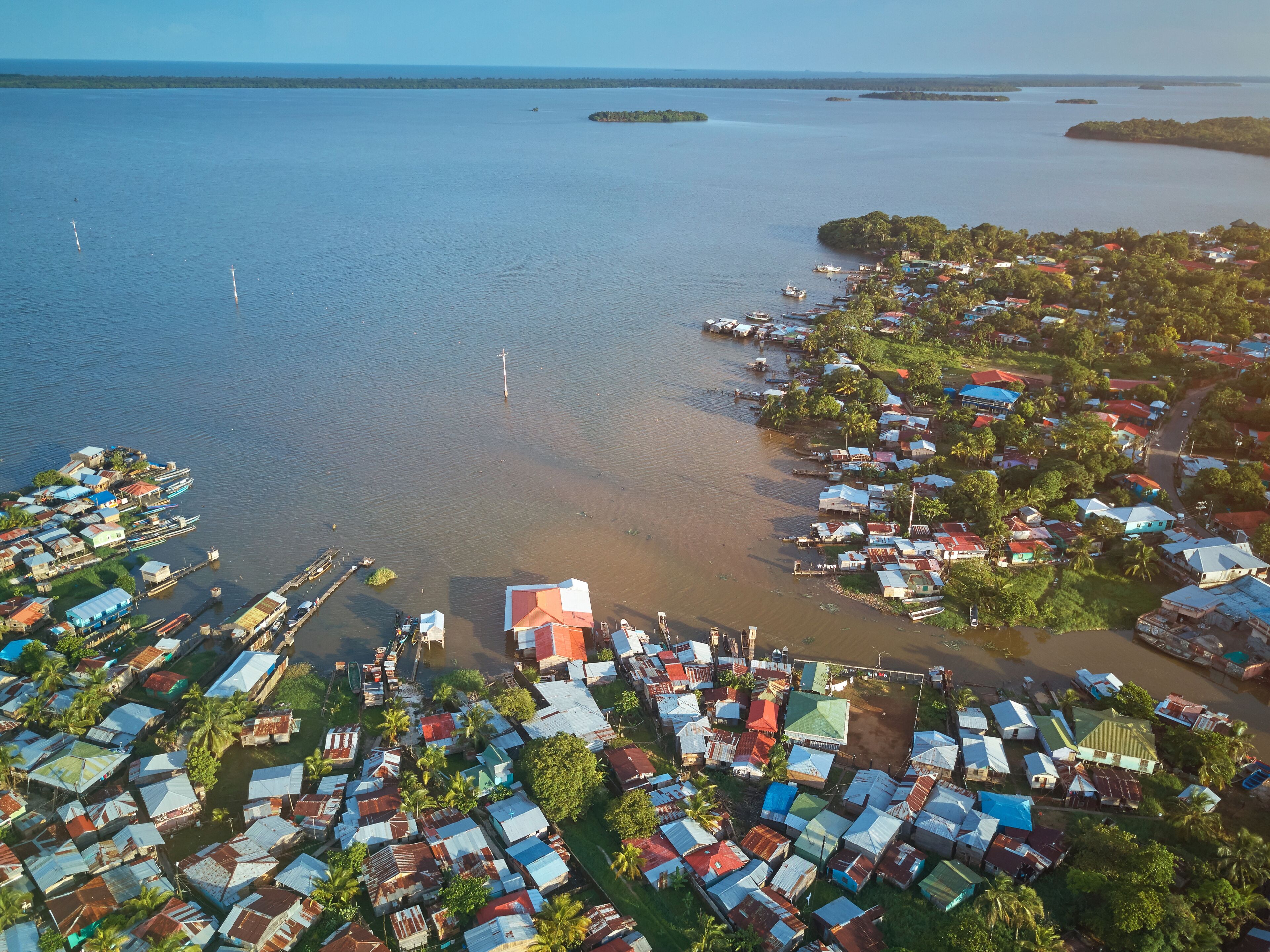 An aerial view of a coastal village with houses, boats, and a clear view of the surrounding water and islands.