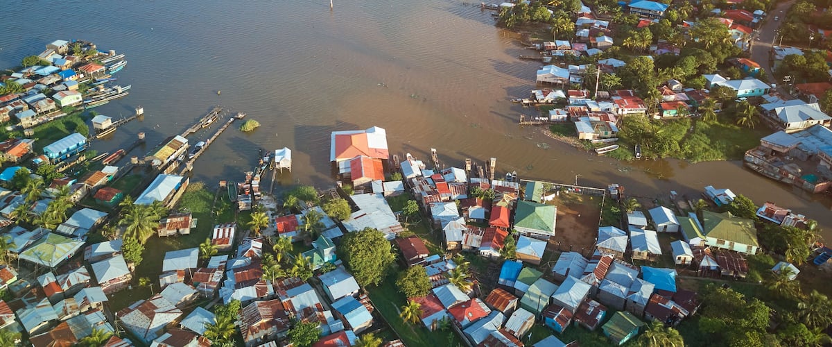 An aerial view of a coastal village with houses, boats, and a clear view of the surrounding water and islands.