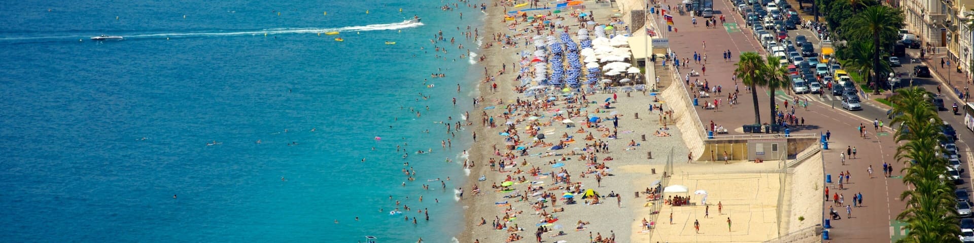 A crowded beach with a clear blue sea, a red balloon, and a busy promenade lined with buildings.