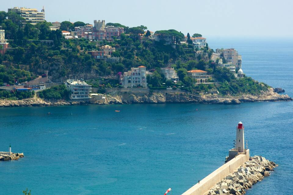 A coastal town with buildings on a hillside, a lighthouse, and the sea.