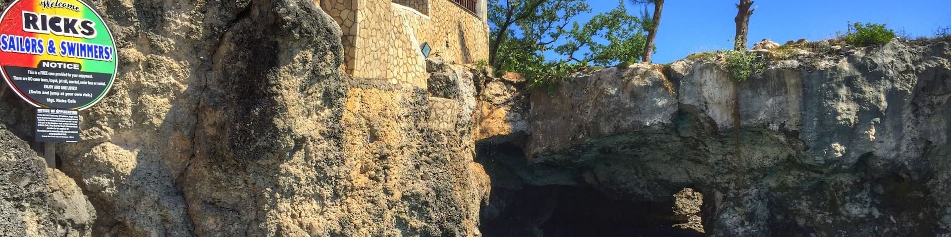 A rocky cliff with a café named 'Ricks Café 1974' and a sign for 'Ricks Sailors & Swimmers'.