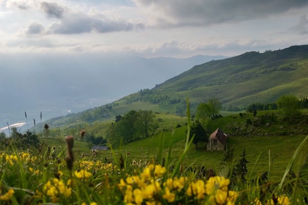 Un paysage rural caractérisé par des collines douces, une petite maison en pierre et une vue lointaine sur une étendue d’eau.