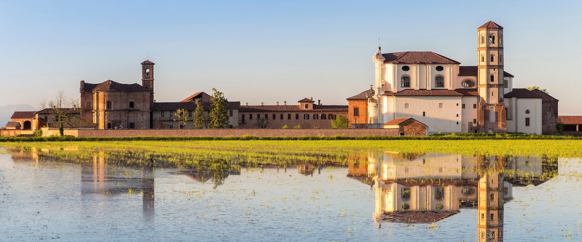 A historic building complex with a prominent bell tower and reflection in a water body.