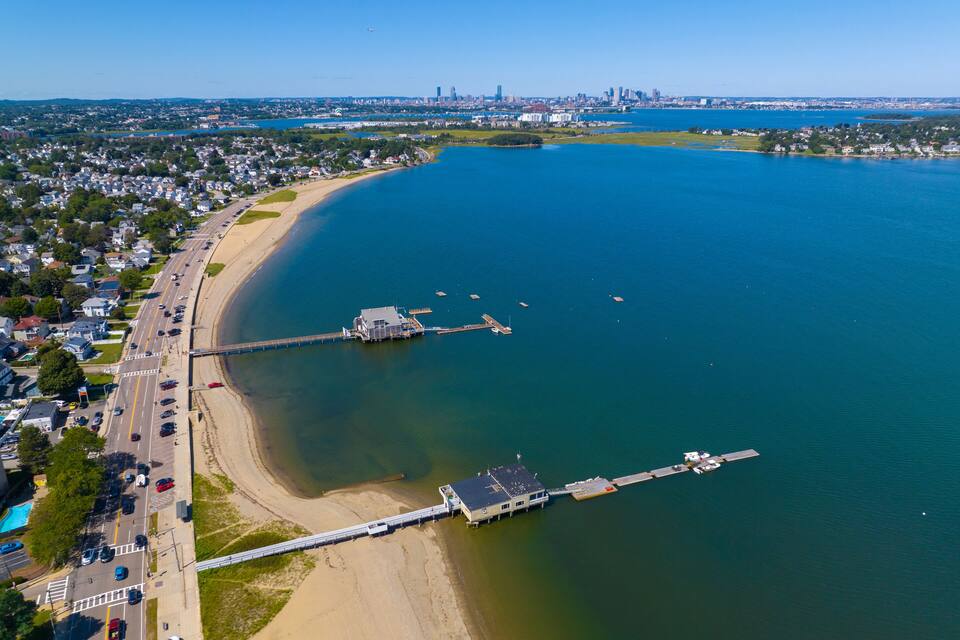 Vista aèria d'una ciutat costanera amb un pont destacat, una marina i un cel blau clar.