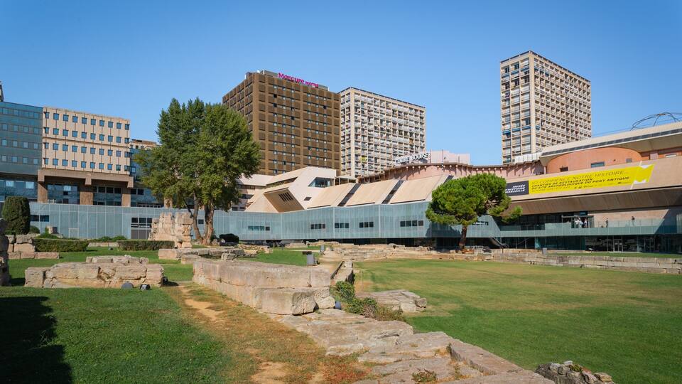 A modern building with a sign for the Mercure Hotel, surrounded by ancient ruins and tall residential buildings.