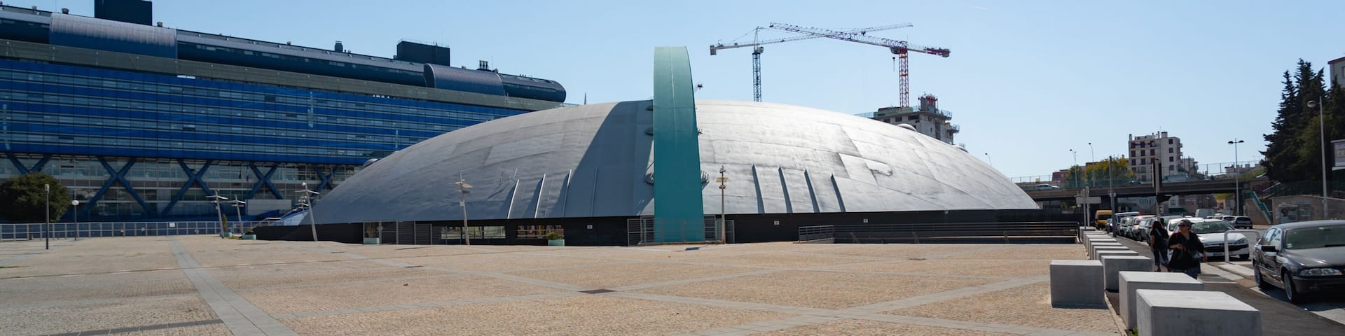 A modern stadium with a large dome and a blue building in the background.