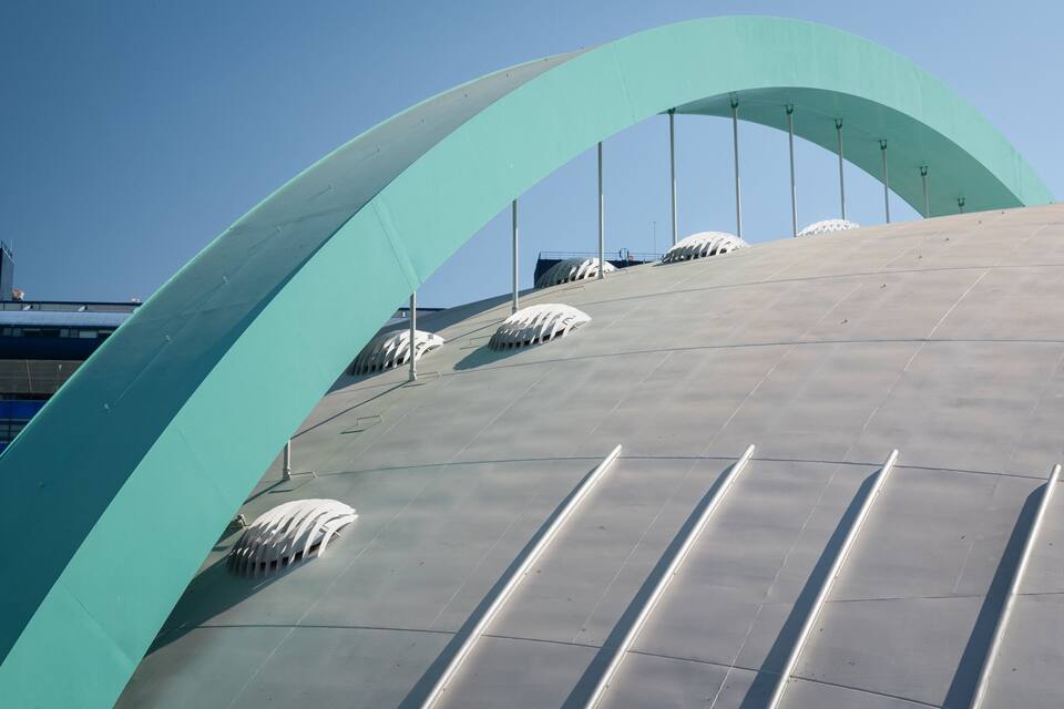 A large, curved architectural structure with a light blue arch and a grey surface.