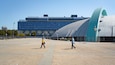 A modern architectural complex with a large blue building and a curved metallic structure.